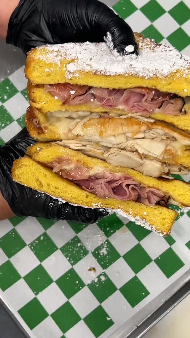 Frisco's Monte Cristo sandwich, golden French toast bread filled with ham and melted cheese, dusted with powdered sugar, served on green-and-white checkered deli paper